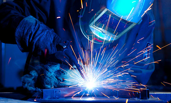 Worker with welding mask engaged in metal fabrication while sparks fly